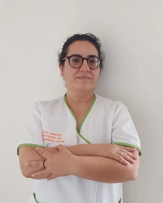 Ana Maria Eufrásio, equipa técnica, de farda branca da associação e óculos, a olhar para a câmara.