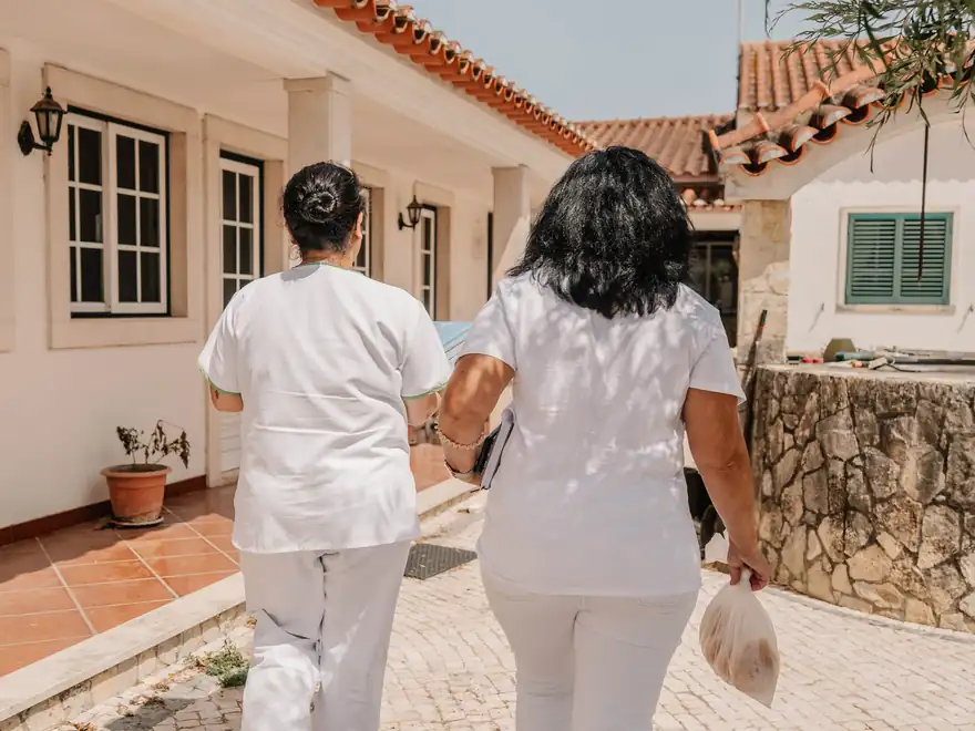 Duas profissionais da associação, de costas, a caminhar por uma rua entre casas.