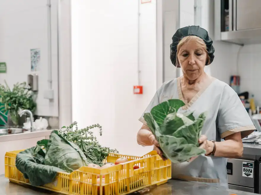 Na cozinha, uma cozinheira prepara as couves vindas da horta, ainda na caixa.