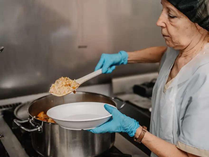 Uma cozinheira serve arroz de frango de uma panela para o prato.