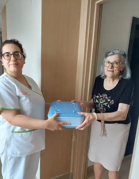 Uma auxiliar da associação entrega uma caixa térmica com a refeição a uma senhora idosa, à porta de casa.